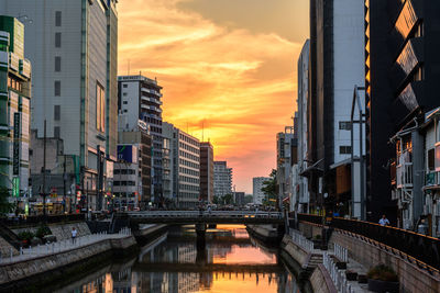 Bridge over river by buildings against sky during sunset