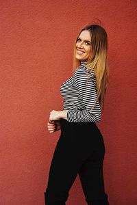 Portrait of smiling young woman standing against wall