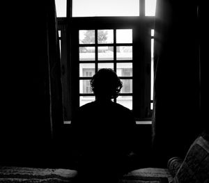 Rear view of silhouette man sitting in window