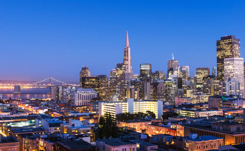 Illuminated buildings in city against blue sky