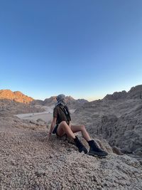 Rear view of woman sitting on rock against sky