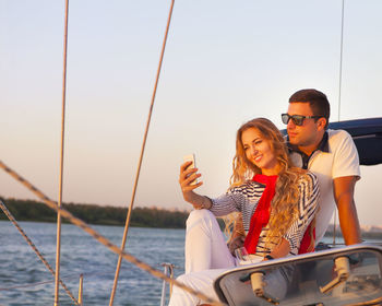 Young couple sitting on boat against sky