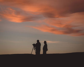 Silhouette people photographing on field during sunset