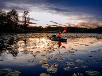 Rear view of man kayaking at lake against cloudy sky during sunset