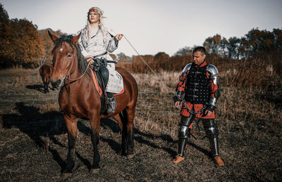 Woman riding horse with man standing on land