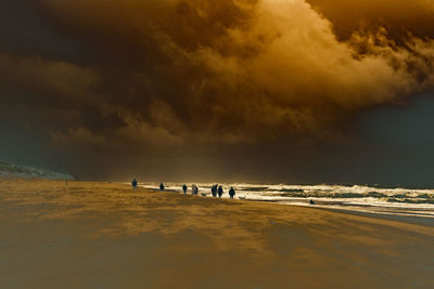 People on beach against dramatic sky during sunset