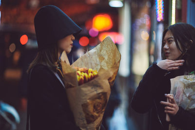 Young woman holding ice cream standing at night in city