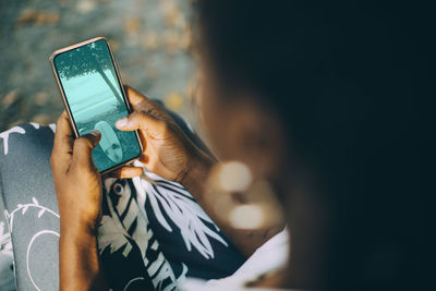 High angle view of young woman looking at beach photograph on smart phone