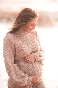Pregnant woman wearing knitted comfy sweater holding tummy over sea outdoors close up. motherhood. 