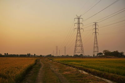 Electricity pylon over rural field against sky during sunset