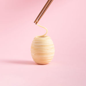 Spaghetti rolled in the shape of easter eggs and wooden chopsticks isolated on a pink background.