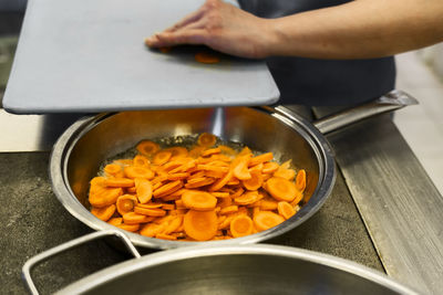 A cook prepares lunch in a fast food cafeteria. fry the carrots in a pan.