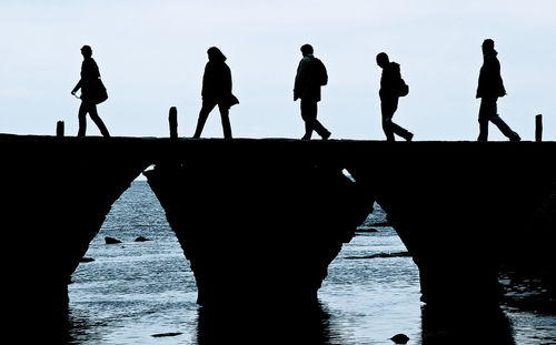 Silhouette people walking on bridge over sea against sky