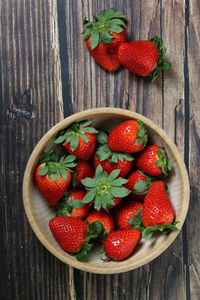 Spring strawberries inside rustic wooden bowl, with wood effect vinyl background