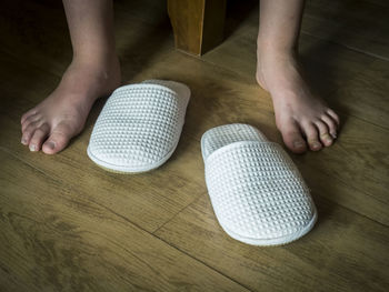 Low section of woman by slippers on hardwood floor at home