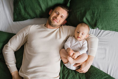 A cheerful, beautiful newly-made dad and a charming six-month-old baby lie together 