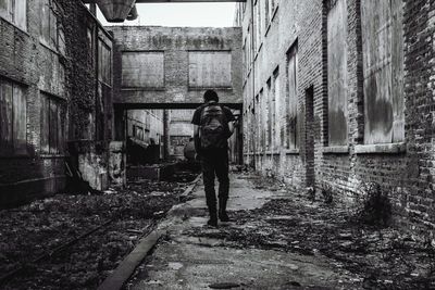 Rear view of man walking amidst abandoned buildings