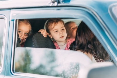 Cheerful little sisters sitting in blue car and feeling happy for an exciting family trip outside