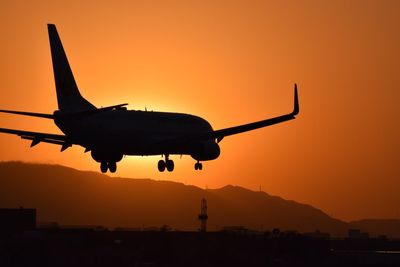 Silhouette airplane landing at airport runway during sunset