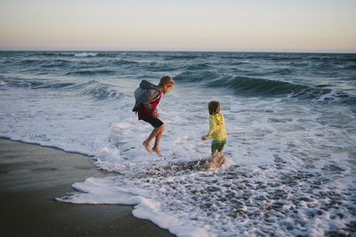 Siblings playing on shore at beach during sunset