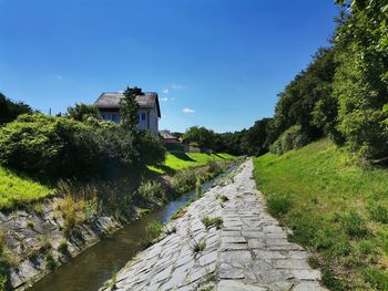 Footpath amidst buildings against clear blue sky