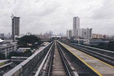 Railway tracks in city against cloudy sky
