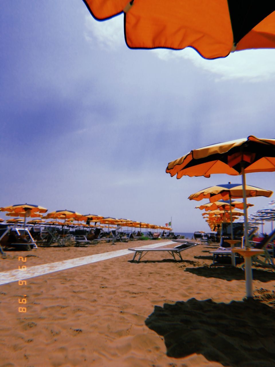 sky, beach, sand, land, nature, water, parasol, incidental people, sea, sunshade, architecture, built structure, beach umbrella, shade, cloud - sky, protection, outdoors, umbrella, horizon over water, wind