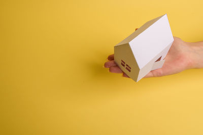 Close-up of hand holding paper against yellow wall