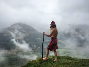 Man standing on mountain against cloudy sky in foggy weather