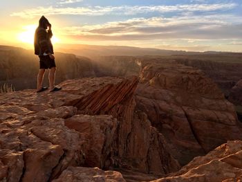 Woman standing on rock against sky during sunset