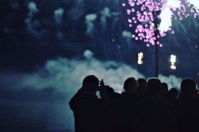 Silhouette of people photographing sea against sky at night