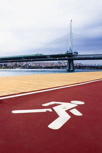 Road sign by bridge against sky