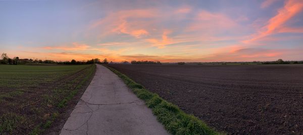 Empty road amidst field against sky during sunset