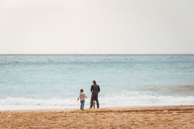 Rear view of men on beach against sky