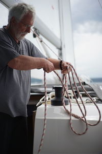 Senior man working on sailboat against sky