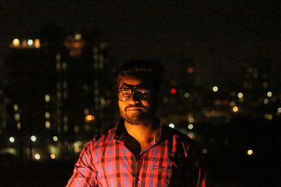 Portrait of young man against illuminated city at night