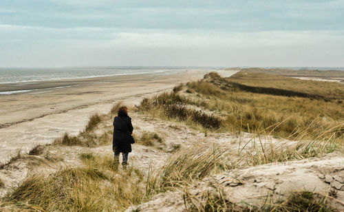 Rear view of man walking on beach against sky