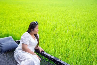 Asian woman in white dress looking at side lay down on hammock net over the rice field