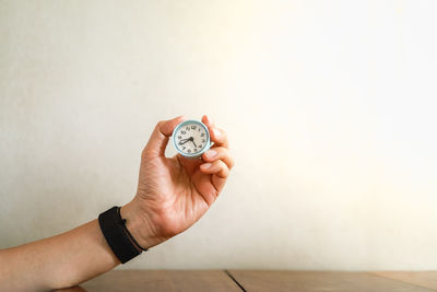 Close-up of hand holding clock against wall