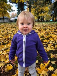 Portrait of cute toddler girl standing on field against trees during autumn