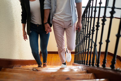 From above anonymous man and woman in casual clothes holding hands and walking up steps at home