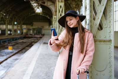 Happy young woman on platform of railway station in pink coat and black hat