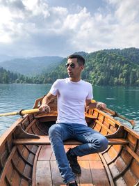 Young man sitting on boat in lake against sky