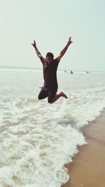 Man with arms raised jumping at beach