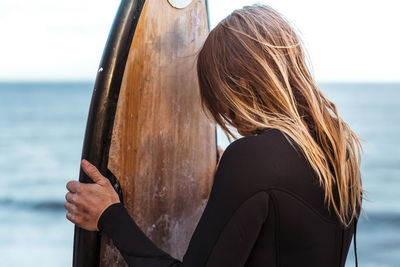 Woman wearing wetsuit while holding surfboard at beach