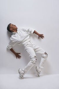 Cheerful young african american woman in stylish white wear and sneakers leaning back on light background