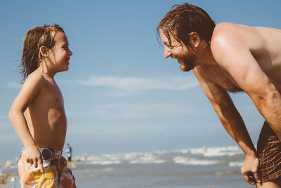 Happy father and son at beach against sky