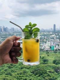 Close-up of hand holding drink in glass against cityscape 