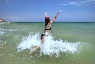 Woman jumping in sea against blue sky