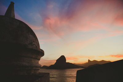 Silhouette rocks by sea against sky during sunset